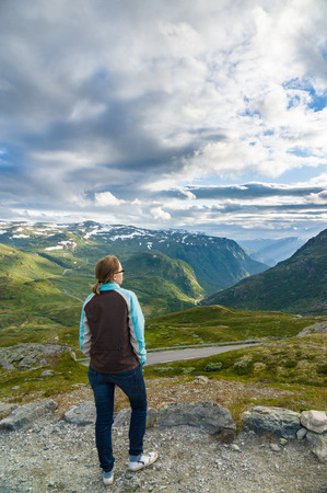 Young lady standing on top of the mountain and looking on mountain valley belowの写真素材