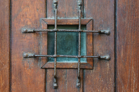 Small square window with grate in old style wooden door, confinement concept