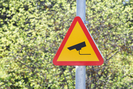 CCTV sign on a post with greenery in the background. Security camera video surveillance symbol