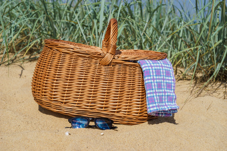 Picnic basket with blue white checkered napkin and sunglasses on sandy beach. Weekend break conceptの写真素材
