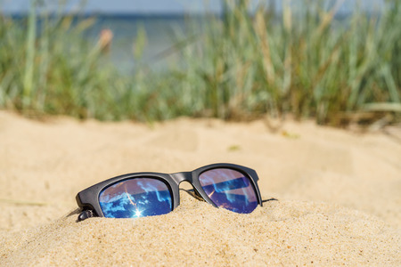 Reflecting sunglasses on sandy beach. Sea and grass on blurred backgroundの写真素材