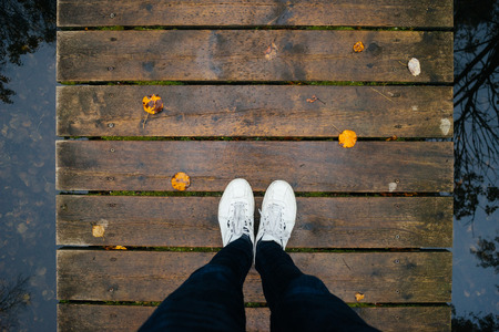 Top view male legs in sneakers on wooden bridge by fall time, tree reflection on water. Autumn conceptの写真素材