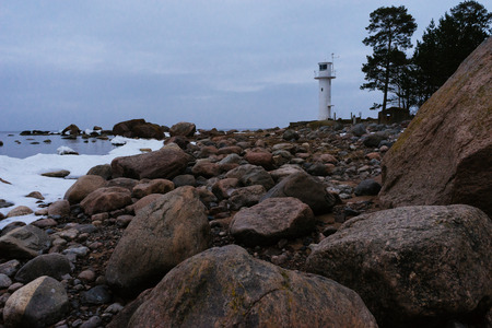 Stony coast of Baltic sea and small lighthouse by winterの写真素材