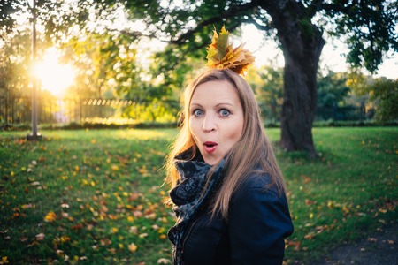 Emotional young woman with bunch of leaves looking surprised in autumnal park. Fall season conceptの写真素材