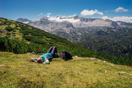 Young female hiker lying on grassy slope. Mountains and glacier on backgroundの写真素材