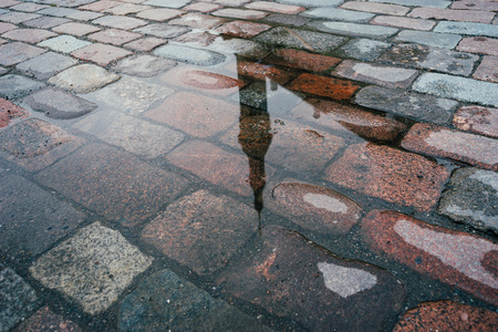 Townhall spire reflection in puddle on cobblestone pavementの写真素材