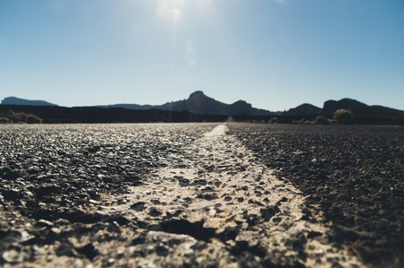 Empty desert road with mountains silhouette on background sunflares, from ground shotの写真素材