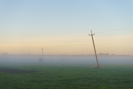 Rural scenery with old power line in thick fog morning. Summer countryside landscapeの写真素材