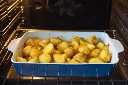 Baked potatoes with curcuma and other spices in roasting pan. Oven on backgroundの写真素材
