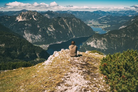 Young man sitting on the edge of mountain and enjoying spectacular view. Vintage toned imageの写真素材