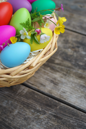 Basket with colorful eggs and springtime flowers on wooden table. Happy easter backgroundの写真素材