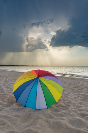 Multicolored umbrella on the beach against dramatic stormy cloudsの写真素材