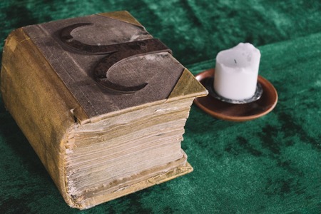 Old heavy book and candle on the medieval table, diagonal view