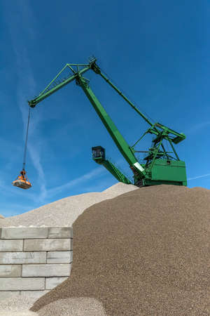 Green harbor crane pours sand and gravel onto a hillの写真素材