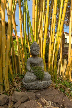 Buddha sculpture made of stone in the front of a bamboo in the gardenの写真素材