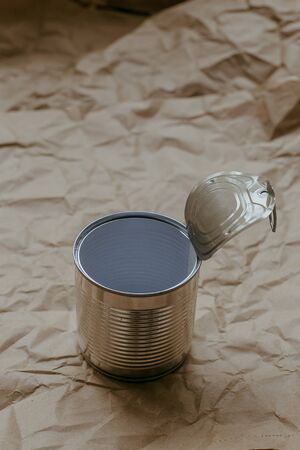 Used iron tin can on a plain crumpled brown kraft paper background. Environmental pollution concept, used trash. Copyspace.の写真素材