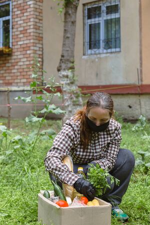 Woman delivering donations box with food during Covid 19 outbreak.Feme volunteer collects food in a box standing on the grassの写真素材