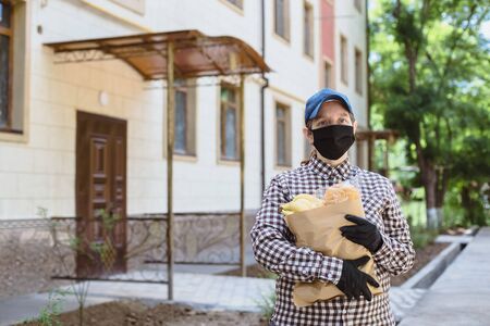 A young woman delivers food in a paper bag. The girl is wearing a protective medical mask and gloves.の写真素材