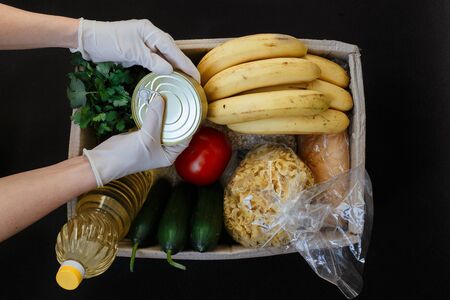 women's hands in rubber gloves fill the box with essential food. Donation box with food.の写真素材