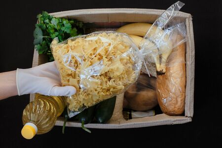 Volunteer collecting food into donation box indoors.Top view of a food box on a black backgroundの写真素材