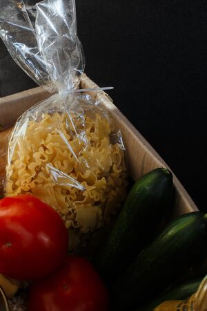 Noodles, pasta in package lie in a box. Nearby are red tomatoes and green cucumbers. Raw materials for cooking. There is a place for textの写真素材