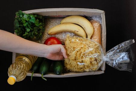 Volunteer collecting food into donation box indoors.Top view of a food box on a black backgroundの写真素材