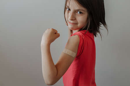 Portrait of a young girl shows arm with patch, after having the vaccine against Coronavirus Covid-19 immunizing - Child bares shoulder after injectionの写真素材