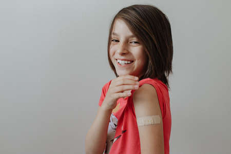 Portrait of a young girl shows arm with patch, after having the vaccine against Coronavirus Covid-19 immunizing - Child bares shoulder after injectionの写真素材