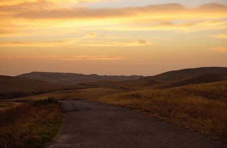Beautiful desert view of country road among autumn yellow brown fields during sunset time. Warm...