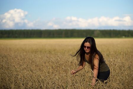 Young woman in the middle of beige wheat field. Girl with long hair. Waist-deep in ears of wheat,...