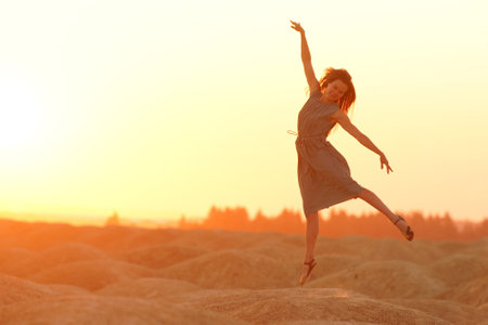Elegant woman with long hair in long dress dancing elegant on sand in desert. Sunrise, backlight...