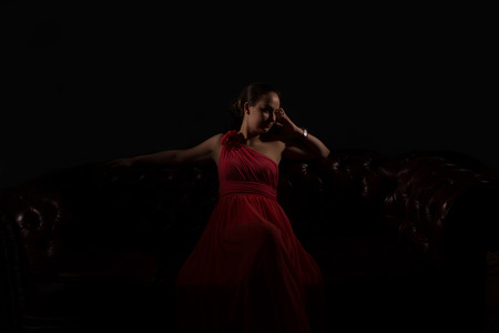 Beautiful woman in red evening dress in dark environmentの写真素材