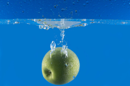 Fresh apple falling in water splash on blue backgroundの写真素材