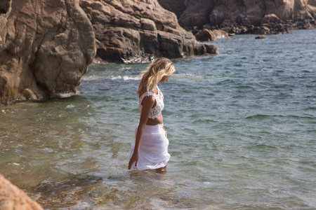 Sexy lady in wet white lace dress on rocky coast.の写真素材