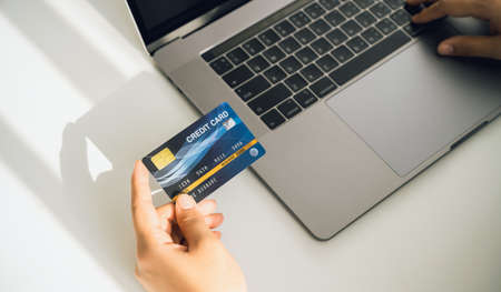 Woman's hand holding a credit card and using a laptop for online shopping on a white desk.の写真素材