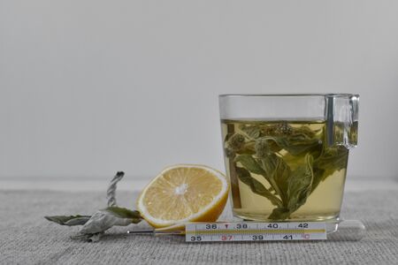 Mint tea with lemon. Thermometer in front of a glass of warming drink. Dry mint grass.