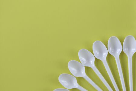 White plastic spoons on a yellow background in the bottom right corner with a place for text.の写真素材