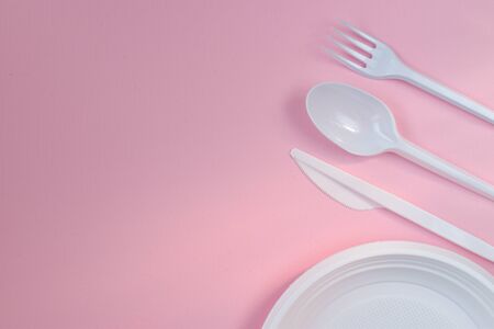 Plastic white utensils on a pink background from the right.