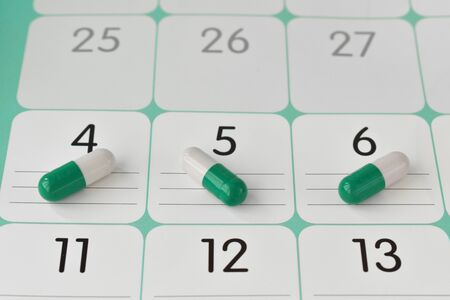 Three white-green capsules in a calendar view from the top.の写真素材