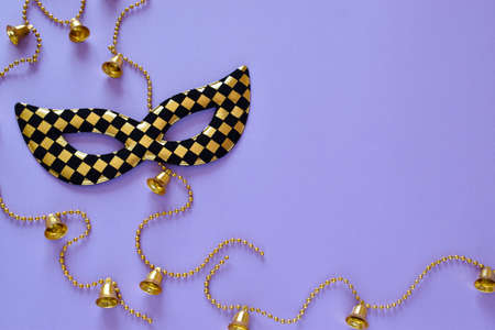 Mask and beads with bells on a purple background on the left side. Flat layout