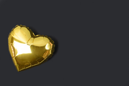 Gold foil balloon in the shape of a heart on a black background. Inflatable metal heart. Valentines Day. Fathers Day. Birthday. Flat lay Top view. A copy of the space.の写真素材