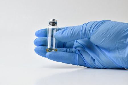 A hand in blue gloves holds the vials of the vaccine isolated on a white. Copy space.