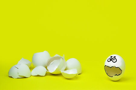 A lonely white egg with a sad face stands next to a mountain of shells on a yellow background.の写真素材