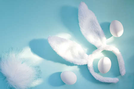 Bunny ears and tail lie among white chicken eggs on a light blue background. Easter. Carnival.
