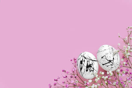Two white eggs in black spots and flowers on a pink background with a copy of the space. Easter....