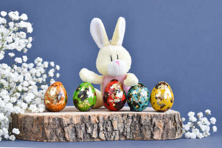 A rabbit with colored eggs sits on a stump. Easter.