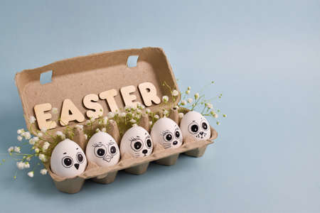 Chicken eggs drawn in a box with faces on a blue background. Easter. Carnival.の写真素材