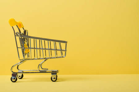 A miniature supermarket cart on a yellow background. Purchases. Minimalism.