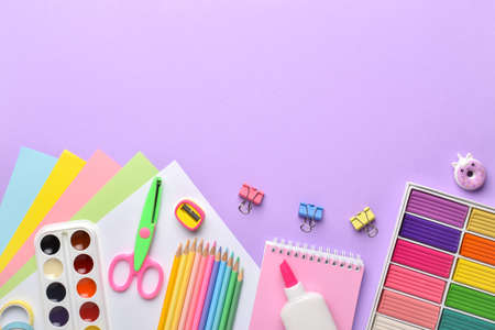 A frame of pastel-colored school supplies on a purple background, a place for text. Flat layout, top...