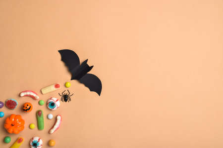 A bat flies and behind it various sweets on an orange background with a place for text. Background for the Halloween holiday. Flat layout, top view, a place to copy. Happy Halloween.の写真素材